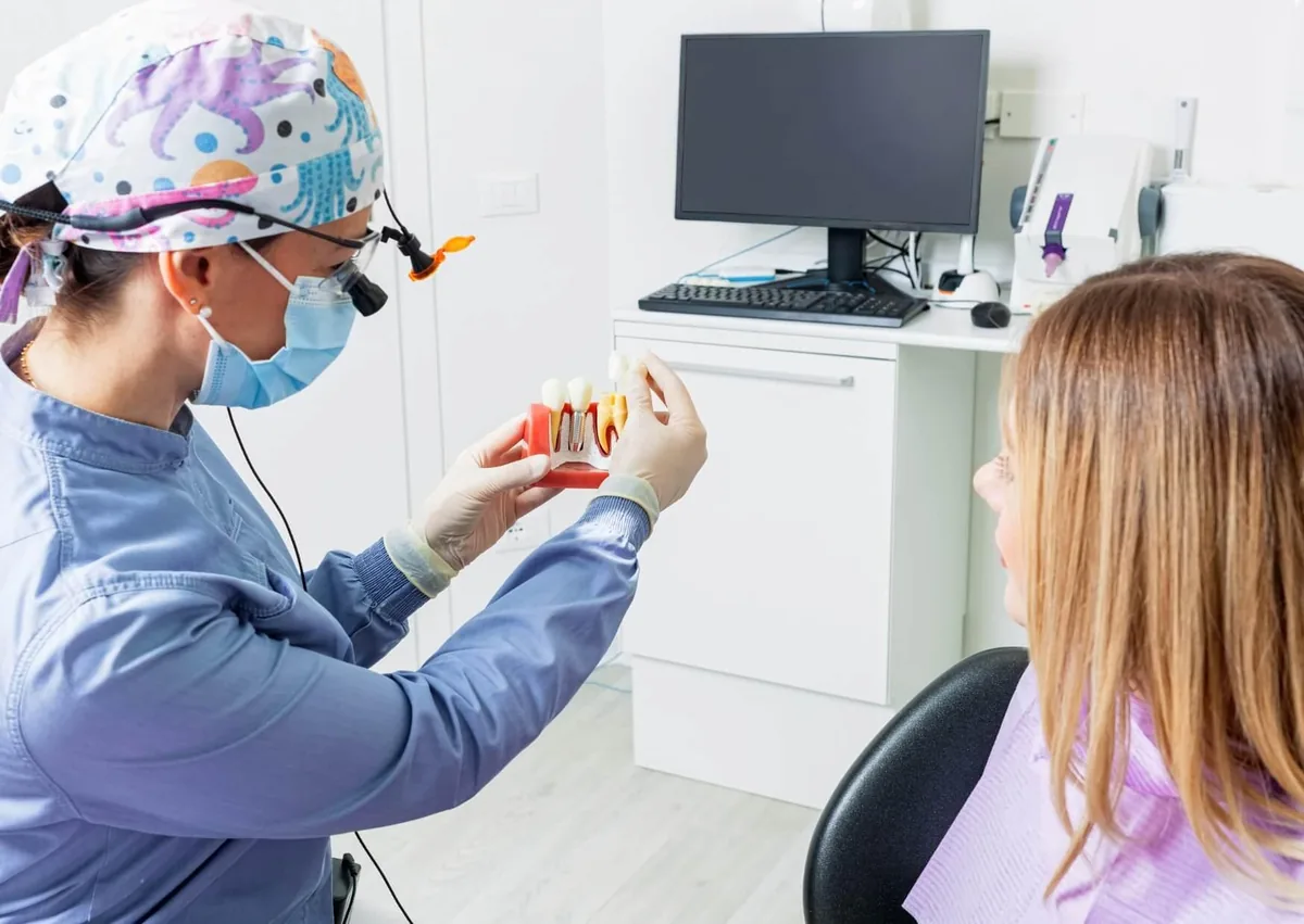 Dentist explaining a single tooth implant model to a patient during a consultation about treatment and cost.