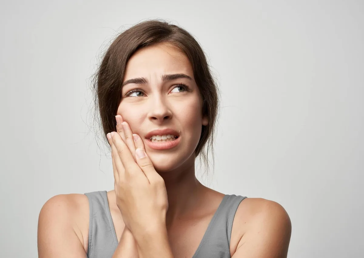 Woman experiencing dental implant pain while chewing and holding the side of her jaw.